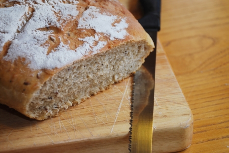 A loaf of home-baked sourdough bread on a wooden chopping board on a wooden table with a large...