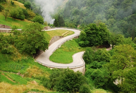 A view of a winding country road in the Carnic Alps near Paularo in the north eastern Italian region of Friuli  A small fire can be seen near the side of the road where a farmer is burning grasses の写真素材