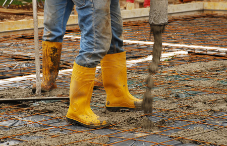 Builders pour concrete onto the foundations of a small house  The foundations comprise steel reinforcement cages and mesh, and radon iglus, and are surrounded by wooden shuttering の写真素材