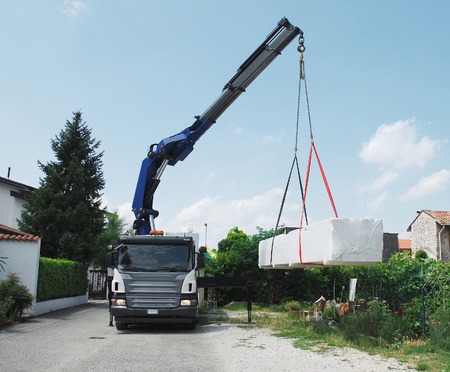 A truck with a telescopic crane delivers packages containing a wood  fir  block house, a pre-cut wooden house which is assembled on-siteの写真素材