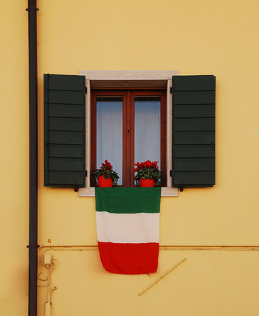 An Italian flag - Il Tricolore - hangs out of the window of an old rural village buildingの写真素材