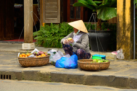 Hoi An, Vietnam - December 20th 2017. A street vendor prepares fruit while waiting for customers on a street in the historic UNESCO listed Vietnamese town of Hoi An.のeditorial素材