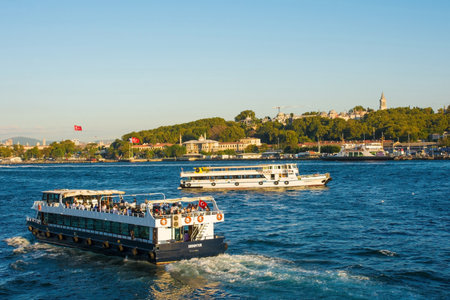 Istanbul, Turkey - September 6th 2019. Boats ferry commuters and tourists to and from the busy Sultanahmet and Eminonu waterfront. The Green Crescent building and Topkapi Palace can be seen in the backgroundのeditorial素材