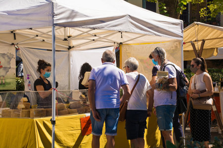 Pienza, Italy - September 6th 2020. Tourists and locals visit a street market just outside the wall of the historic centre of Pienza in Tuscany, Italy, during the COVID-19 pandemic. This cheese stall specialises in mature goat's cheese (pecorino staginatoのeditorial素材