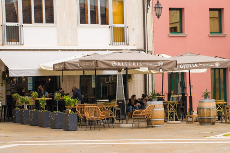 Marano Lagunare, Italy - April 29th 2021. A bar serves a few lunchtime customers willing to brave the unseasonal weather and threat of rain as bars and restaurants are allowed to re-open, outside only, a few days after the third national lockdown is lifteのeditorial素材