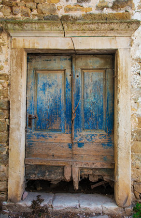 An old wooden door in a derelict stone residential building in the historic medieval village of Buje in Istria, Croatiaの写真素材