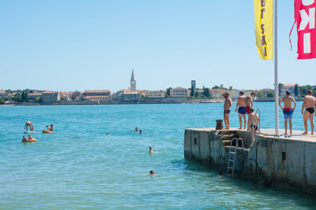 Porec, Croatia- July 10th 2021. Holiday makers and locals use a pier to get into the water at Parentino Beach outside the historic medieval coastal town of Porec in Istria, Croatiaのeditorial素材