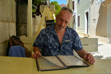 Porec, Croatia- July 10th 2021. A tourist looks at a menu outside a restaurant in historic centre of the medieval coastal town of Porec in Istria, Croatiaのeditorial素材