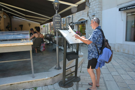 Porec, Croatia- July 10th 2021. A tourist looks at a menu outside a restaurant in historic centre of the medieval coastal town of Porec in Istria, Croatiaのeditorial素材