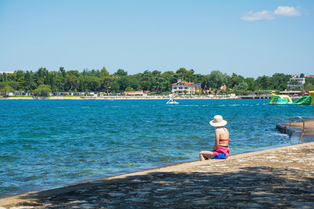 A tourist enjoys the summer sun and sea on the coast just north of the historic centre of Porec on the Istria coast of Croatiaのeditorial素材