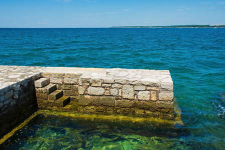 Stone steps into the Adriatic Sea from the coastal path around the historic medieval town of Porec in Istria, Croatiaの写真素材