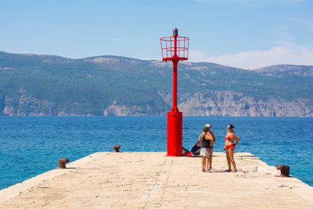 Glavotok, Croatia - 7th September 2021. Tourists talk by the red lighthouse on Glavotok pier during late summer, Krk Island in Primorje-Gorski Kotar County, western Croatiaのeditorial素材