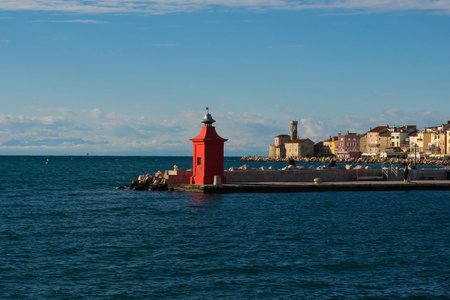 A red lighthouse on the waterfront of the historic medieval town of Piran on the coast of Slovenia. Background right is the Our Lady of Health Church and a 17th century lighthouse towerの写真素材
