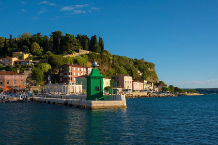 Piran, Slovenia - September 17th 2022. A small green lighthouse on the waterfront of the historic medieval town of Piran on the coast of Sloveniaのeditorial素材