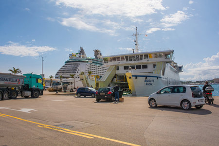 Split, Croatia - May 12th 2023. A roll-on/roll-off ferry going to a nearby island loads vehicles in the port of the historic coastal town of Split in Dalmatia, Croatia. A mega cruise liner is in the backgroundのeditorial素材
