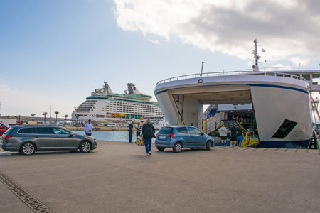 Split, Croatia - May 12th 2023. A roll-on/roll-off ferry going to a nearby island loads vehicles and foot passengers in the port of the historic coastal town of Split in Dalmatia, Croatia. A mega cruise liner is in the backgroundのeditorial素材