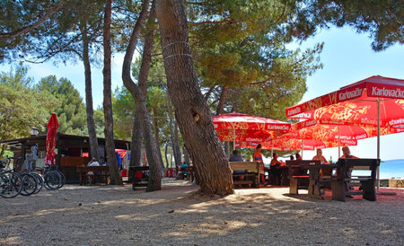 Rovinj, Croatia - July 7th 2023. Customers enjoy food and drink in the shade at Cuvi Beach just south of Rovinj old town in Istria, Croatiaのeditorial素材