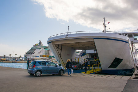 Split, Croatia - May 12th 2023. A roll-on/roll-off ferry going to a nearby island loads vehicles and foot passengers in the port of the historic coastal town of Split in Dalmatia, Croatia. A mega cruise liner is in the backgroundのeditorial素材