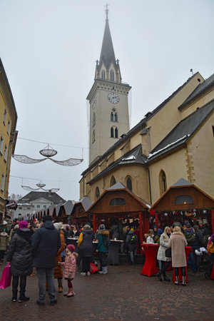 Villach, Austria - December 24th 2022. Christmas market stalls on Hauptplatz street on a slightly foggy Christmas Eve in the historic centre of Villach in Carinthia, Austria. The spire of the parish church of Saint Jacob is in the backgroundのeditorial素材