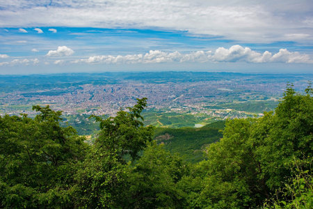 A panoramic view of Tirana, the capital city of Albania, viewed from Mount Dajti in the Skanderbeg Mountains. The lush forested mountain slopes in the foreground contrast against the urban landscapeの写真素材