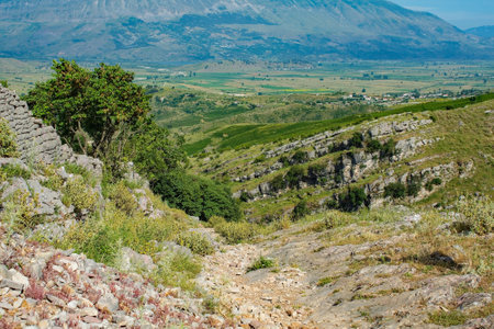 The rugged landscape in the Drino Valley area just outside Gjirokaster, central Albania. An old stone wall foreground left separates different areas of land. A popular area for walking and hiking for locals and tourists alike. June, early summerの写真素材
