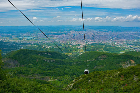A cable car ascends Mount Dajti, offering breathtaking panoramic views of the sprawling urban landscape below and the surrounding green countrysideの写真素材
