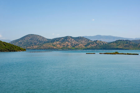 Lake Butrint in Southern Albania, part of the Butrint National Park. A saltwater lagoon connected to the Ionian Sea through the Vivari Channel. It is famous for its rich biodiversity, including rare bird species. Traditional wooden fishing traps or weirs consisting of wooden stakes or poles driven into the shallow waters are seen in the distanceの写真素材