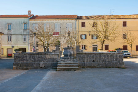 A traditional stone well in the historic village of Svetvincenat in central Istria, Croatia. With a rounded base and curved body, and an iron arch and pulley, it is typical of traditional wells in the region. Adorned by festive Christmas lights. Located in Gradski Trg Squareの写真素材