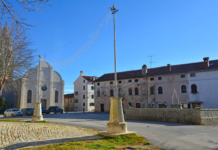 Gradski Trg Square in the village of Svetvincenat in central Istria, Croatia. This Renaissance-era square surrounded by historic stone buildings lies at the heart of the village. Left is the Annunciation of the Blessed Virgin Mary Church, an impressive 16th century parish church with a Renaissance trefoil facade. Called Crkva Navjestenja Marijina in Croatianの写真素材