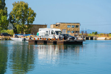 Cars and a motorhome wait to cross the Vivari Channel to the Butrint Archaeological Park, within Butrint National Park in southern Albania, a UNESCO World Heritage Site. They are using a cable ferry, a small manually operated boat system. Also called Kanali i Butrintit or Butrinto River, it links Lake Butrint to the Straits of Corfuの写真素材