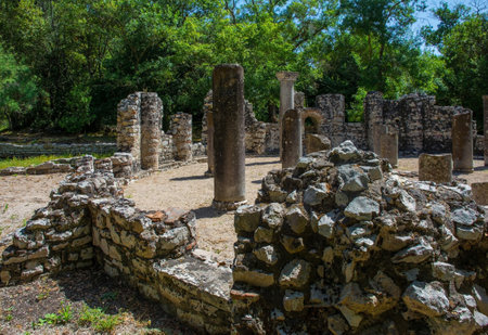 The Baptistry Complex in Butrint Archaeological Park, within Butrint National Park, southern Albania. Dating from between 3rd & 6th centuries, this early Byzantine monument features a large circular design with central cross-shaped baptismal font surrounded by 2 concentric colonnades, each with 8 granite columns which once supported a wooden roof. The floor is adorned with mosaics covered with sand for preservation. There is a fountain in the background wall. In the centre, an Ionic impost capital featuring acanthus leaves and crossesの写真素材