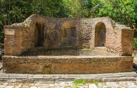 The Nymphaeum in Butrint Archaeological Park, within Butrint National Park, southern Albania. A UNESCO World Heritage Site. A 2nd century monumental Roman fountain formed by a semicircular pool facing east on the street leading to the Tower Gate, with a circular wall and 3 niches, of which the central one had a cloister vault & the lateral ones barrel vaults. Enclosed by a ditch. A public water feature, likely dedicated to nymphs and used for religious or decorative purposesの写真素材