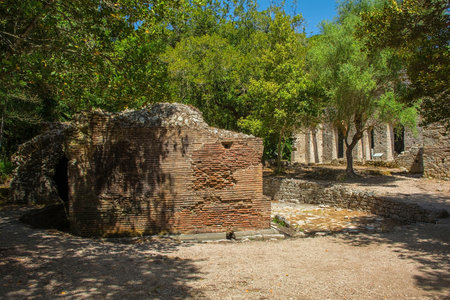 A side view of the Nymphaeum in Butrint Archaeological Park, within Butrint National Park, southern Albania. A UNESCO World Heritage Site. A 2nd century monumental Roman fountain formed by a semicircular pool facing east on the street leading to the Tower Gate, with a circular wall and 3 niches, of which the central one had a cloister vault & the lateral ones barrel vaults. Enclosed by a ditch. A public water feature, likely dedicated to nymphs and used for religious or decorative purposes. The Great Basilica is seen in the backgroundの写真素材
