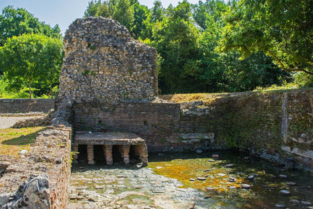 A Roman public bathhouse in Butrint Archaeological Park, within Butrint National Park, southern Albania. A UNESCO World Heritage Site. Located next to the Roman Forum, hypocaust heating allowed the circulation of warm air to heat baths, the brick pillars supported the floor. It featured a series of rooms for hot, warm and cold bathing (caldarium, tepidarium, frigidarium). The baths served as a social and recreational hubの写真素材