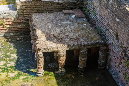 A Roman public bathhouse in Butrint Archaeological Park, within Butrint National Park, southern Albania. A UNESCO World Heritage Site. Located next to the Roman Forum, hypocaust heating allowed the circulation of warm air to heat baths, the brick pillars supported the floor. It featured a series of rooms for hot, warm and cold bathing (caldarium, tepidarium, frigidarium). The baths served as a social and recreational hubの写真素材