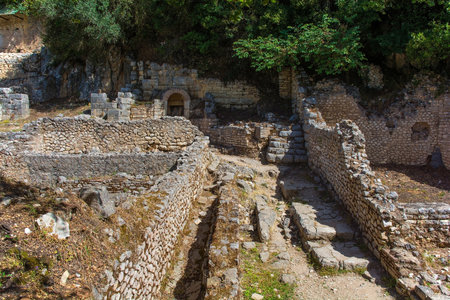 The Roman Forum in Butrint Archaeological Park, within Butrint National Park, southern Albania. A UNESCO World Heritage Site. This was Butrint's civic centre, surrounded by administrative and commercial buildings, and including a marketplace, temples and a basilica. The shrines at the north of the Forum are seen in the background along with the Stoa Church top leftの写真素材
