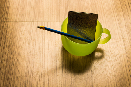 Blue pencil and notebook in a cup of green water on the floor inside the house.の写真素材
