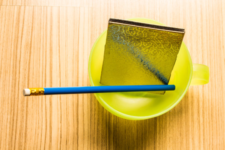 Blue pencil and notebook in a cup of green water on the floor inside the house.の写真素材