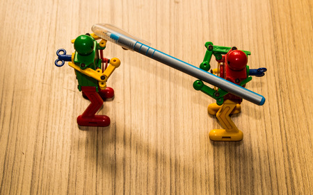 Two small robot holding a pen on the floor, brown wood background.の写真素材