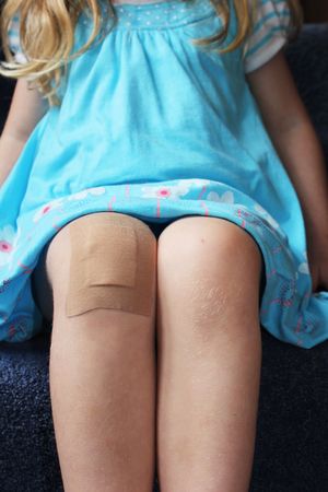 a girl sitting on the stairs with a plaster on her kneeの写真素材