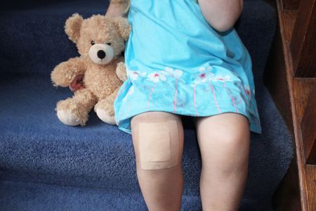 girl with plaster on knee cuddling teddy bear on stairsの写真素材