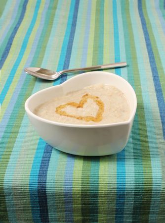 porridge in a heart shaped bowl on a stripey canvas background with a silver spoonの写真素材