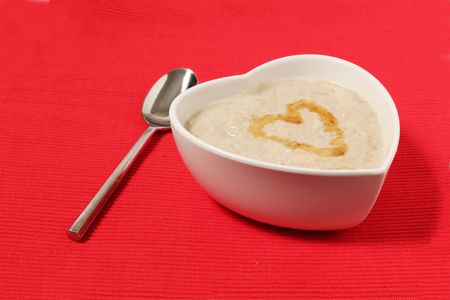 porridge in a heart shape bowl on red canvas background with honeyの写真素材