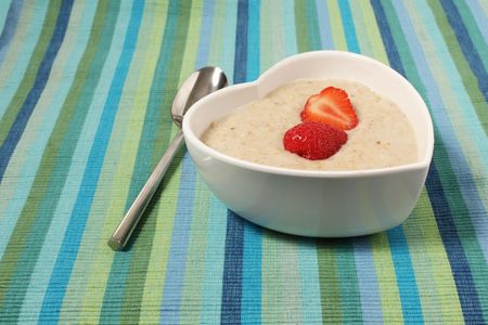 porridge in a heart shaped bowl with strawberries on a stripey canvas table clothの写真素材