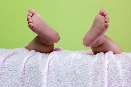 Pair of baby feet dangling on pink towel against green backgroundの写真素材