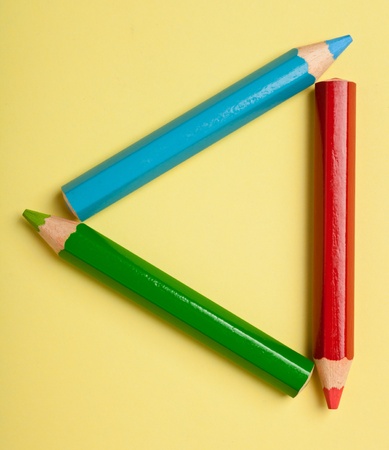 Colorful color pencils forming a triangle frame on a piece of yellow paperの写真素材