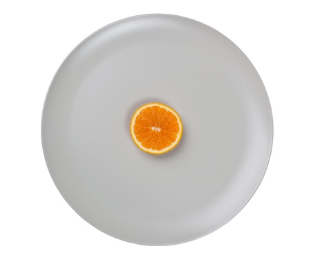 Slice of orange in the center of a big plate isolated on white backgroundの写真素材