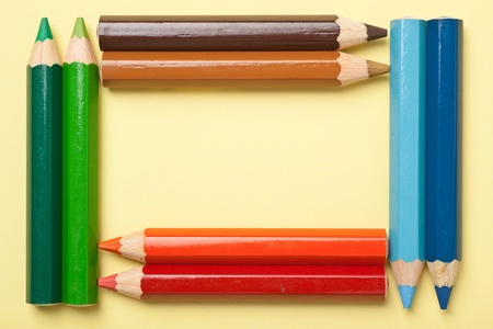 Colorful color pencils forming a rectangle frame on a piece of yellow paperの写真素材