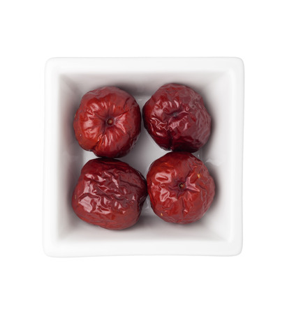 Dried big red jujubes in a square bowl isolated on white backgroundの写真素材
