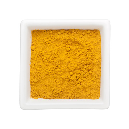 Turmeric powder in a square bowl isolated on white backgroundの写真素材